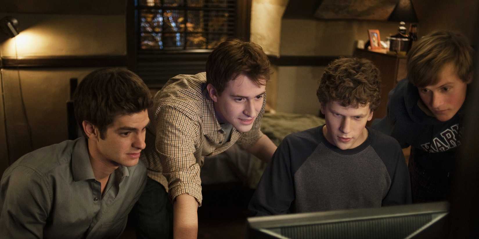 The cast of The Social Network crowded around a computer looking at the screen intently.