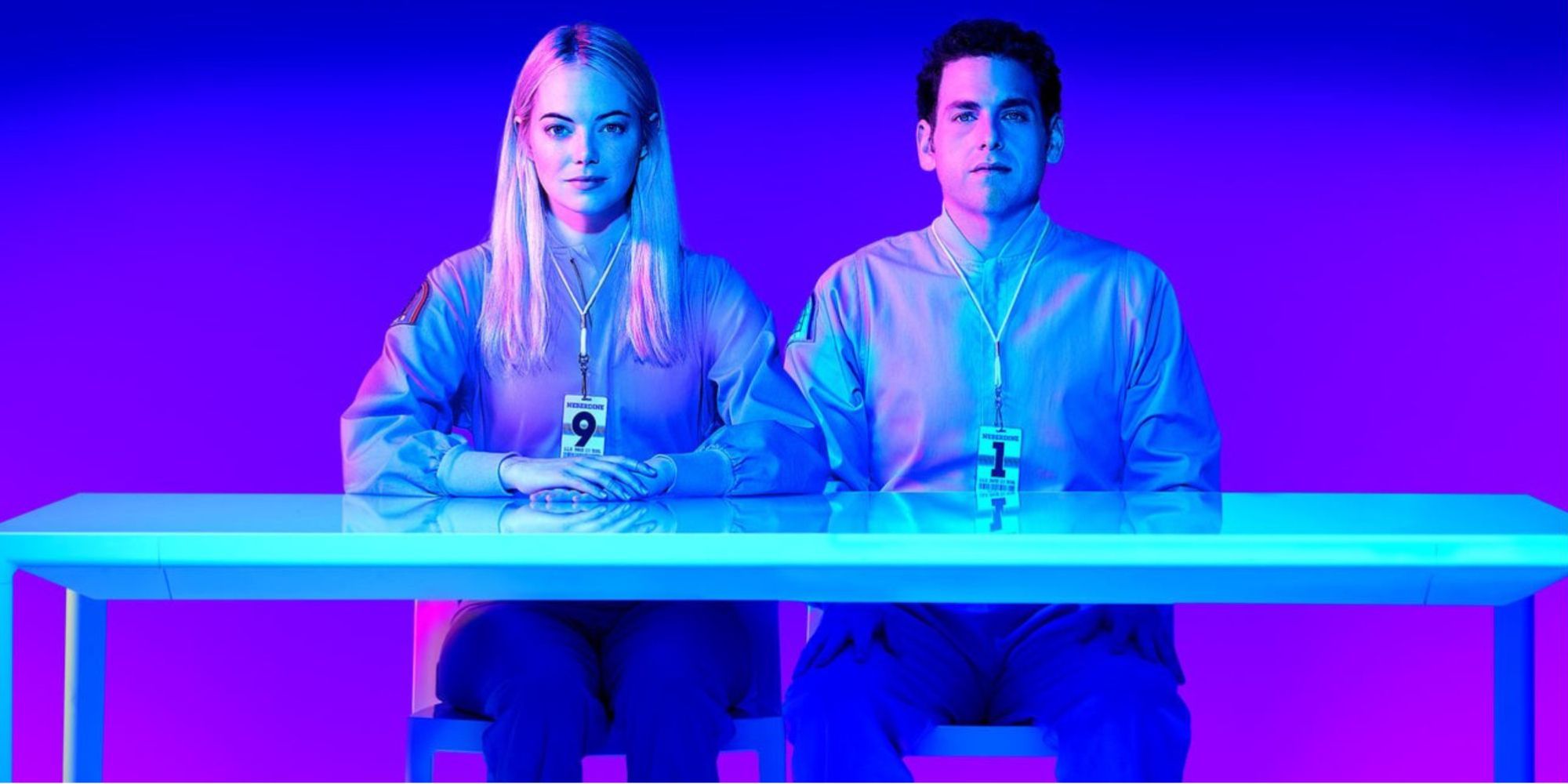 Emma Stone and Jonah Hill in matching uniforms sit at a small table and stare ahead in Maniac, 2018.