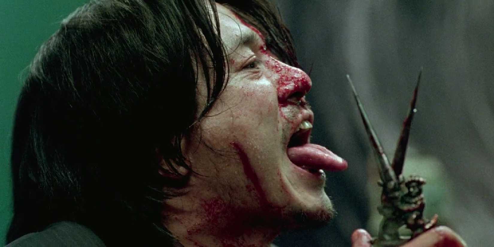 Choi Min-sik sticking his tongue out while raising a pair of scissors in Oldboy