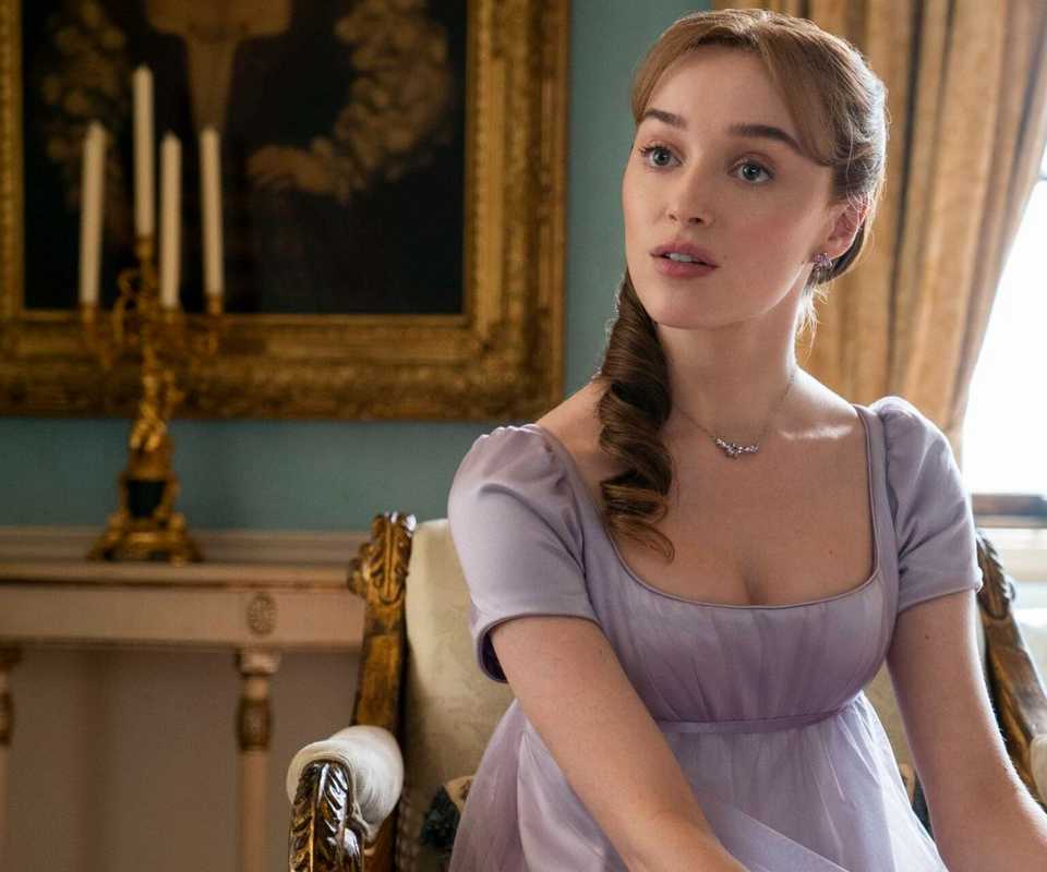 Phoebe Dynevor as Daphne sitting on a chair and looking at someone off-camera in Bridgerton