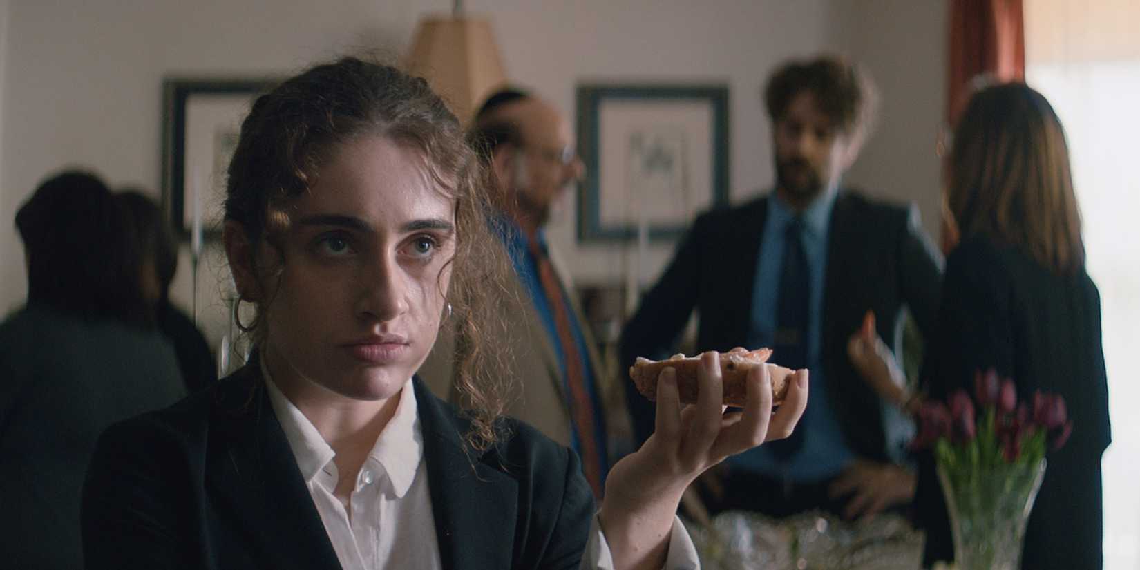  Rachel Sennott looks unimpressed while holding a bagel