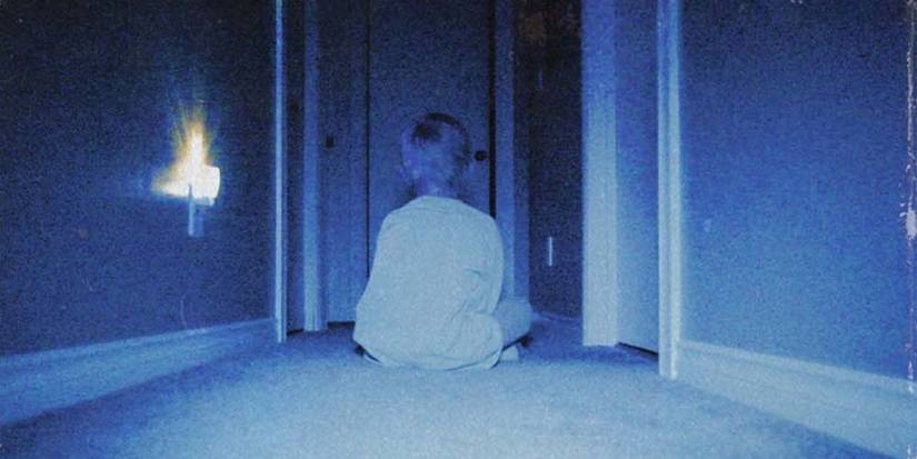 Kevin (Lucas Paul) sits in a hallway in the dark and stares into an empty room in Skinamarink.