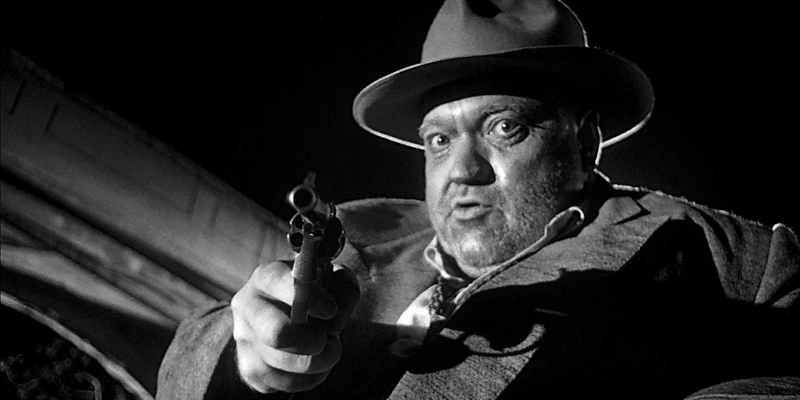 Orson Welles aponta sua arma para alguém fora da câmera em Touch of Evil