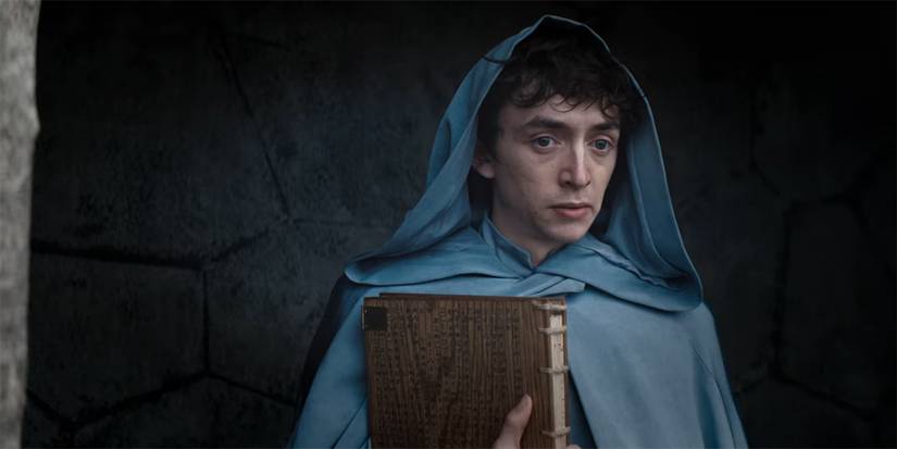 Avallac'h holding abook and looking intently at something off-camera in The Witcher: Blood Origin