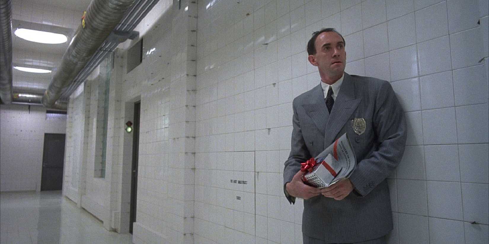Jonathan Pryce standing in a long hallway holding a present and a piece of paper in Brazil.