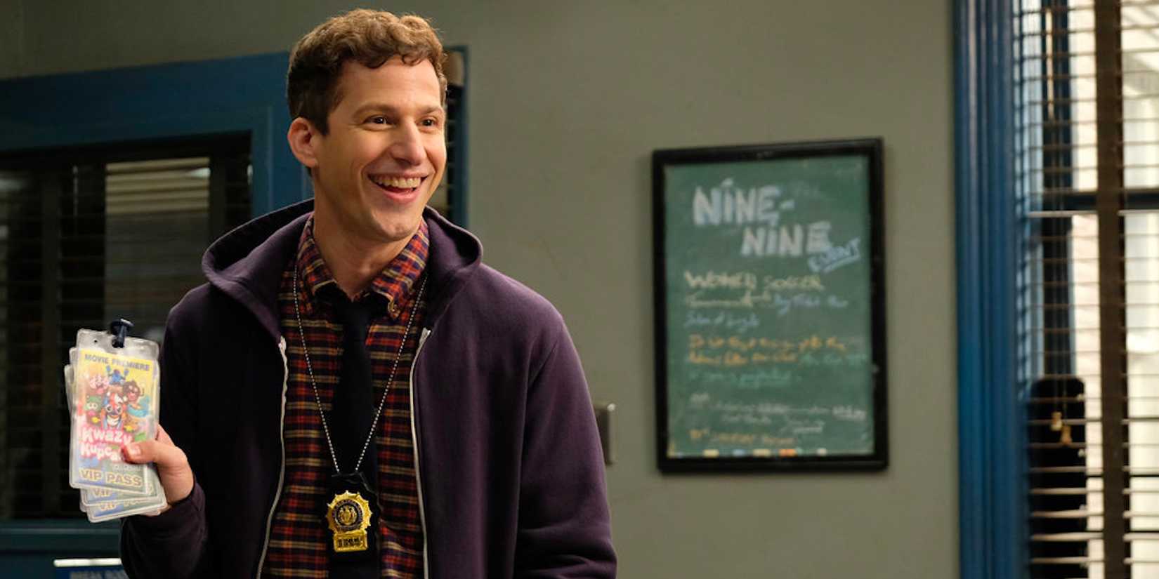 Andy Samberg as Jake Peralta in Brooklyn Nine-Nine smiling while holding tickets.