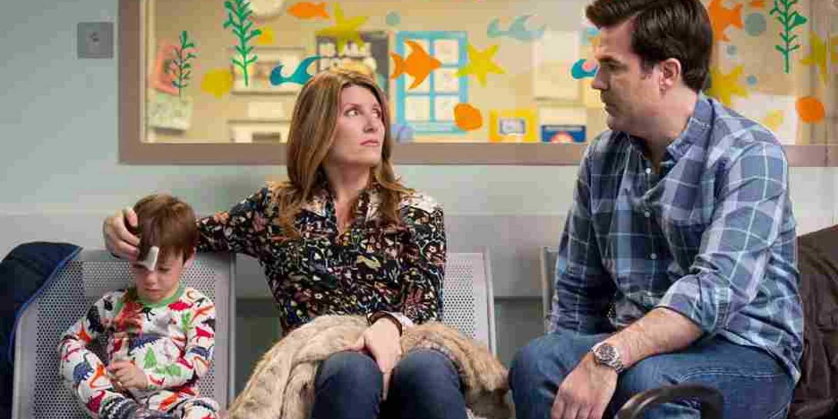 A man (Rob Delaney) and a woman (Sharon Horgan) sitting with a young boy, holding a cloth to his head in Catastrophe.