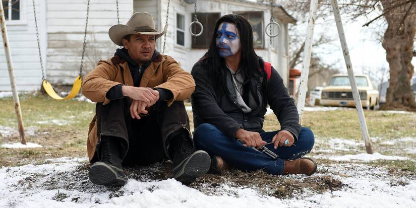 Jeremy Renner dan Gil Birmingham sebagai Cory Lambert dan Martin Hanson duduk di tanah bersalju di Wind River.