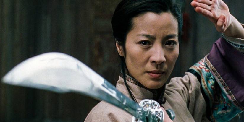 Michelle Yeoh looks determined in a martial arts stance, holding a sword in Crouching Tiger Hidden Dragon.