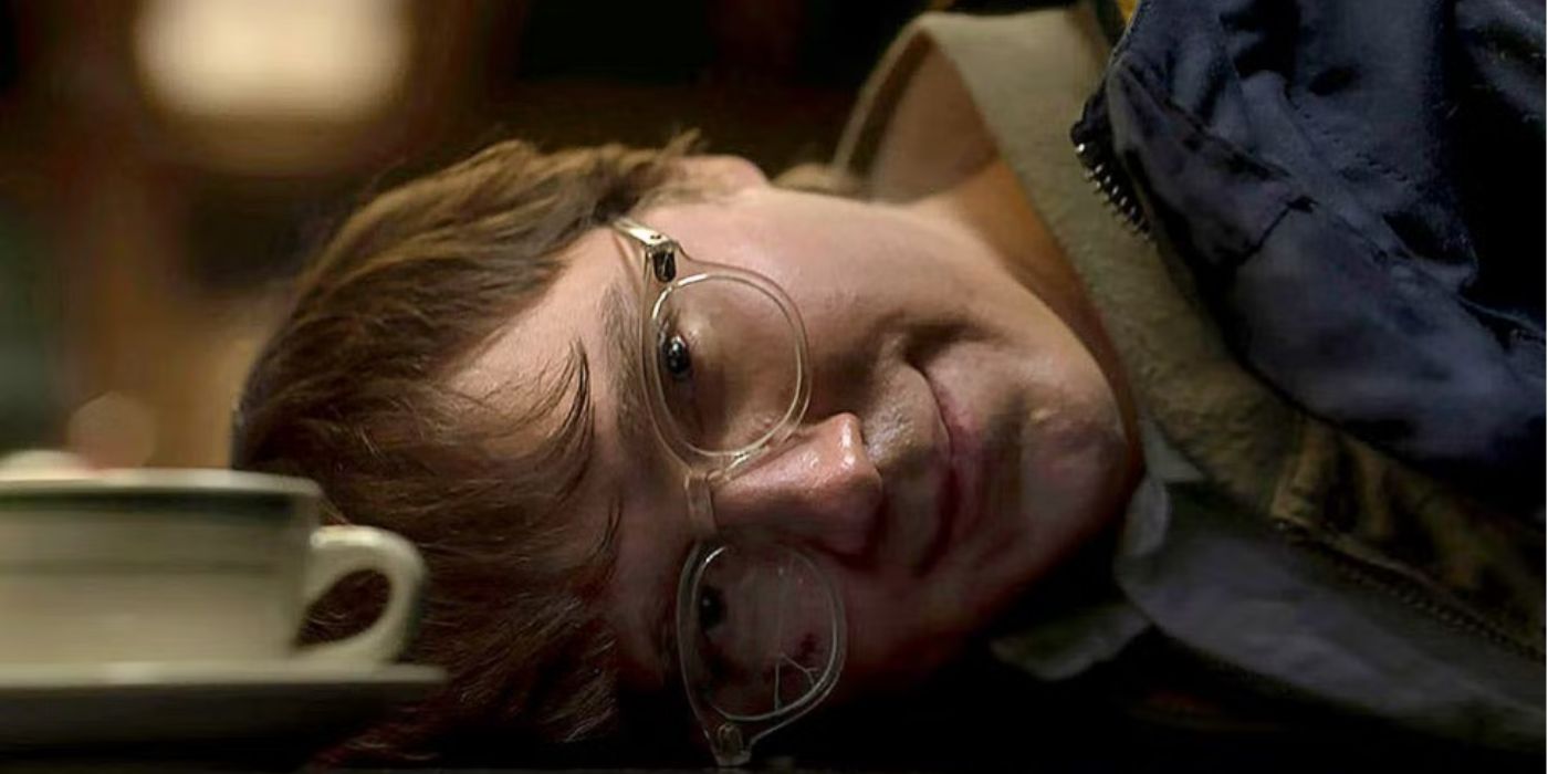 The Riddler, played by Paul Dano, smiling with his head down against the counter as he's arrested