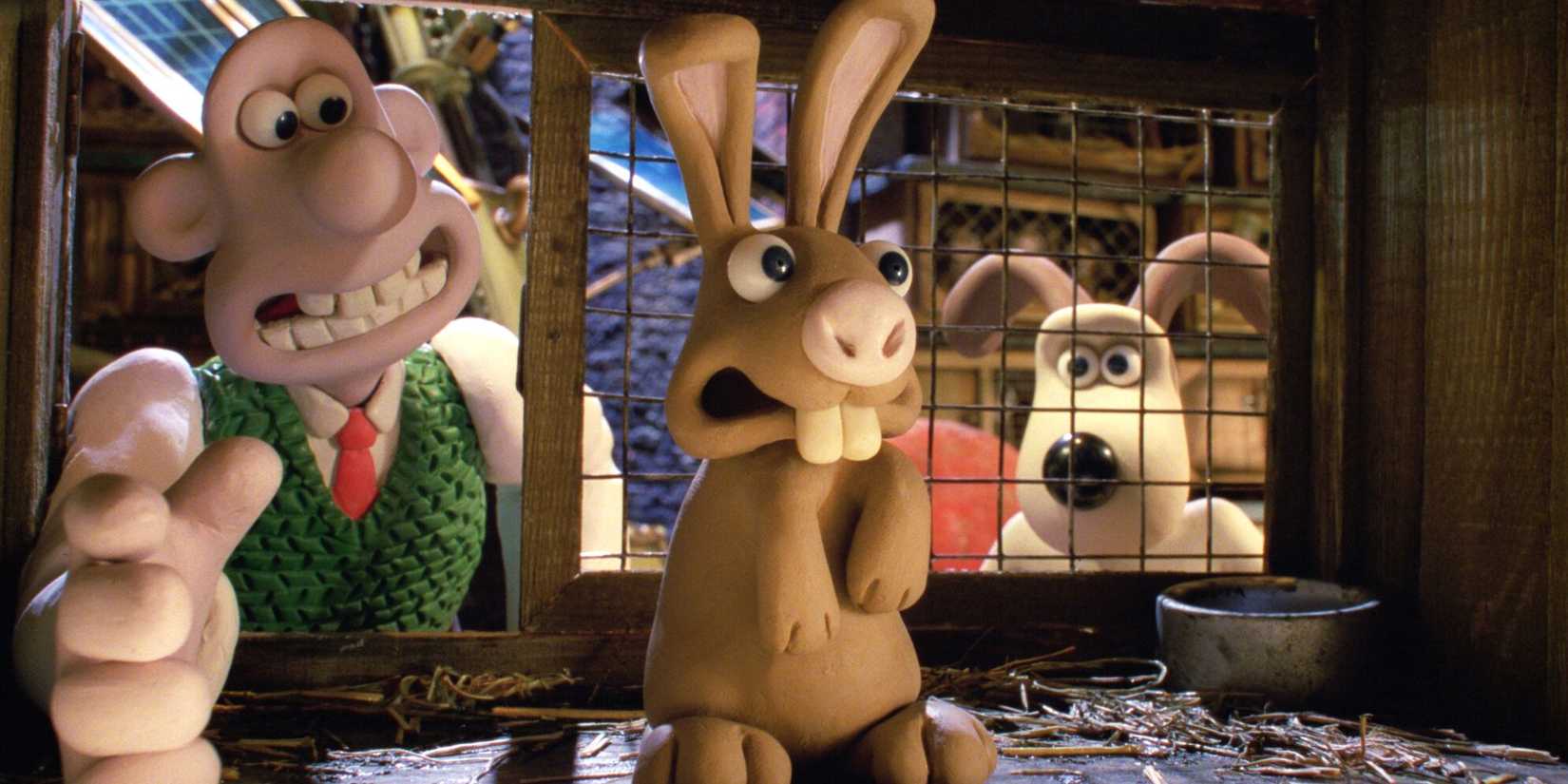 Wallace reaches into a cage for a rabbit, Gromit standing behind him in Curse of the Were-Rabbit