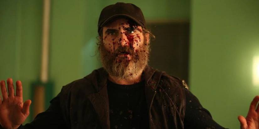 Joe with blood splattered on his face and his hands up in surrender in 'You Were Never Really Here.'