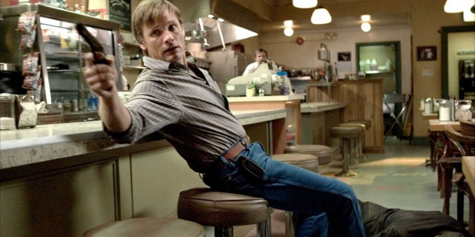 Viggo Mortensen as Tom Stall aiming a gun at someone in his bar in A History of Violence (2005).