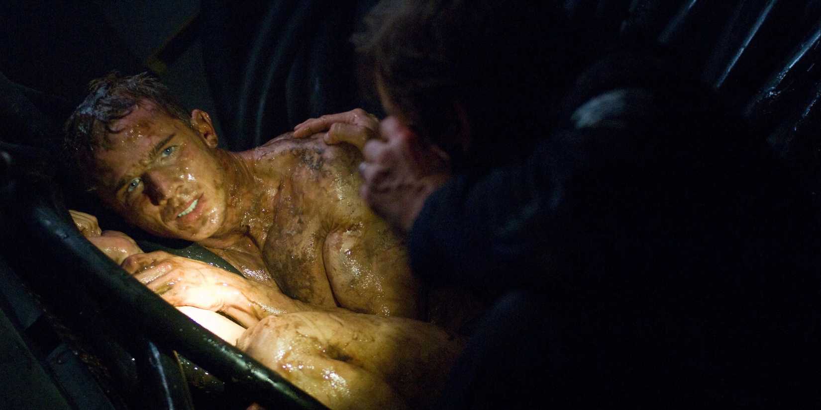 A naked man covered in slime and oil shivers as another man with a flashlight talks to him in Pandorum.