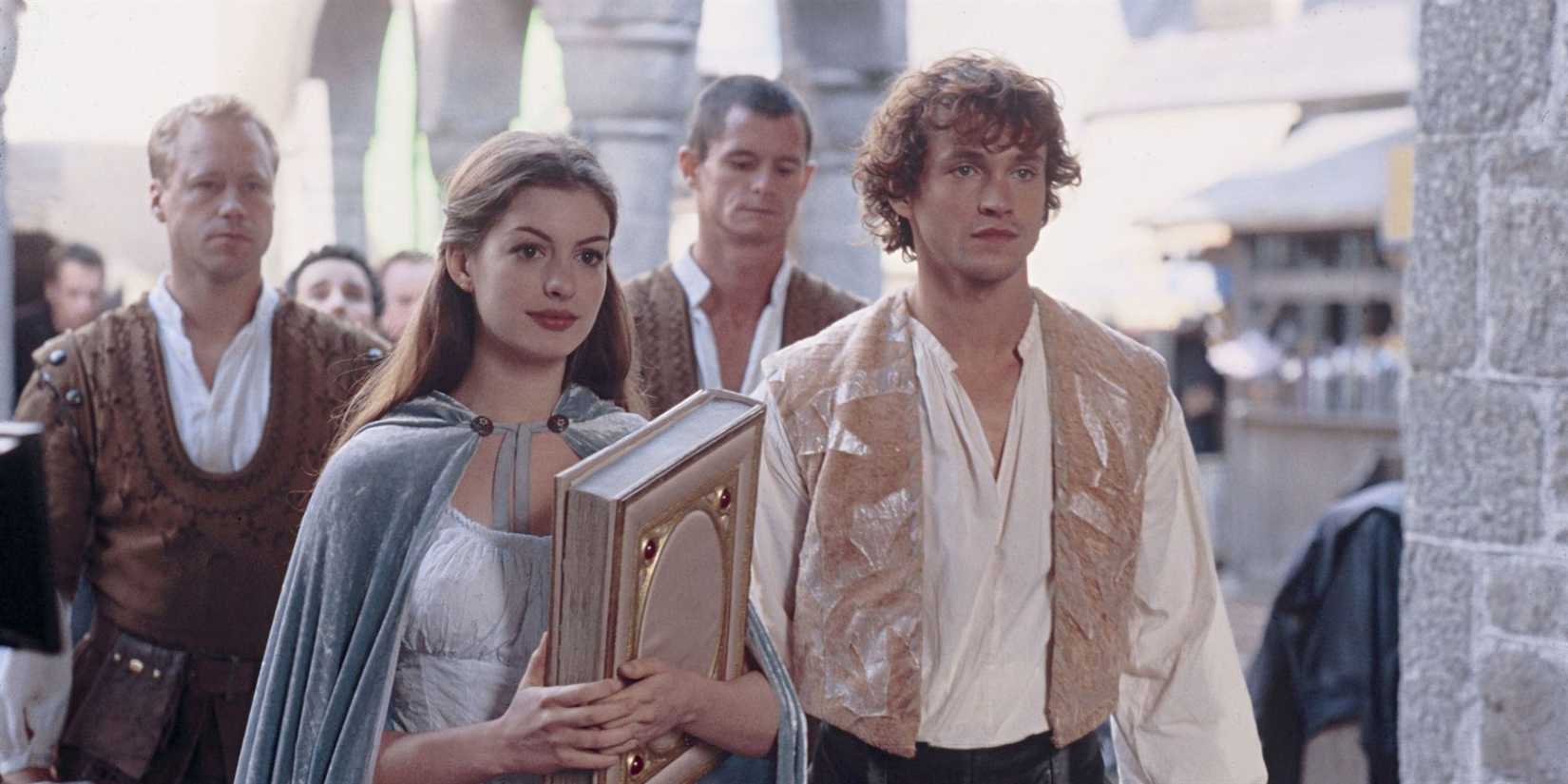 Ella holds a book and stands next to Prince Charmont, both looking ahead in 'Ella Enchanted'.