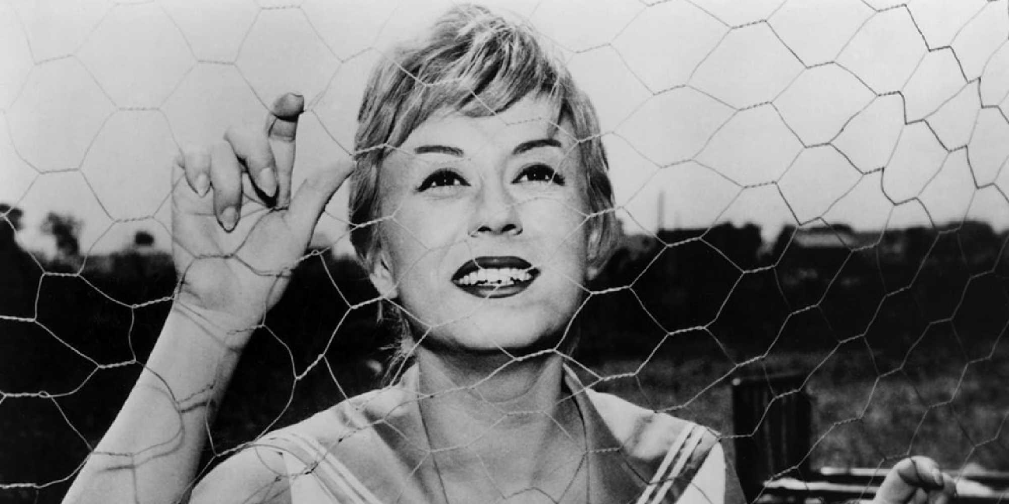 Giulietta Masina behind a wire fence smiling in Nights of Cabiria.