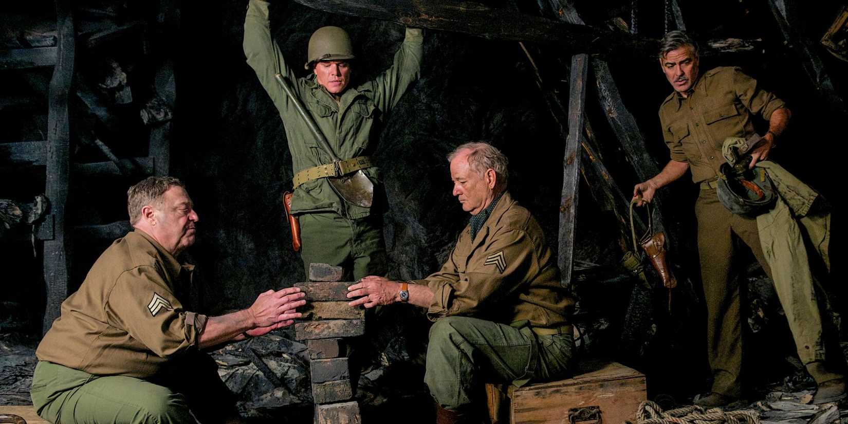 John Goodman and Bill Murray sitting across from each other with a pile of bricks in the middle, Matt Damon standing behind them and George Clooney off to the side in The Monuments Men