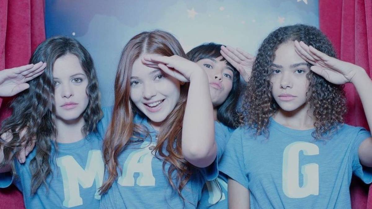 Antonia Gentry as Ginny, Sara Waisglass as Max, Katie Douglas as Abby, and Chelsea Clark as Norah wearing MANG shirts and saluting in a photo booth in Ginny & Georgia Season 1.