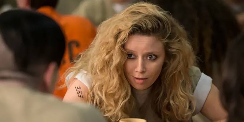 Natasha Lyonne in Orange is the New Black crouched down talking to someone at the table.