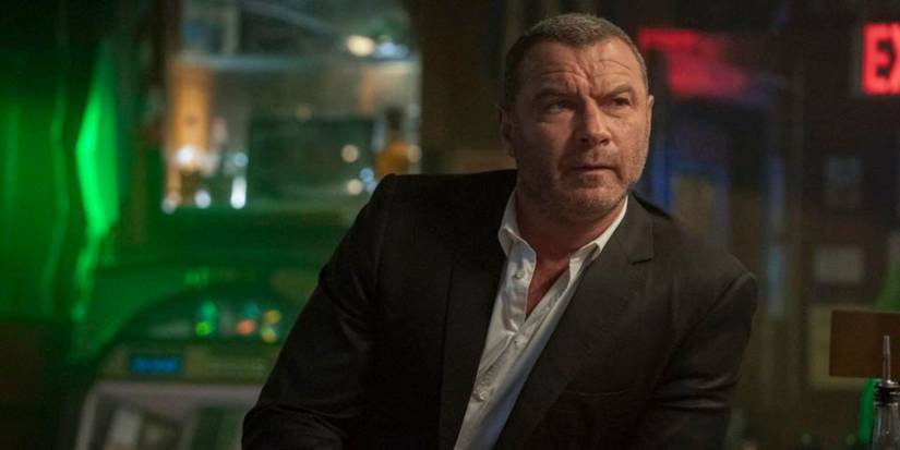 The character Ray Donovan is standing at a bar looking angry in the series Ray Donovan.
