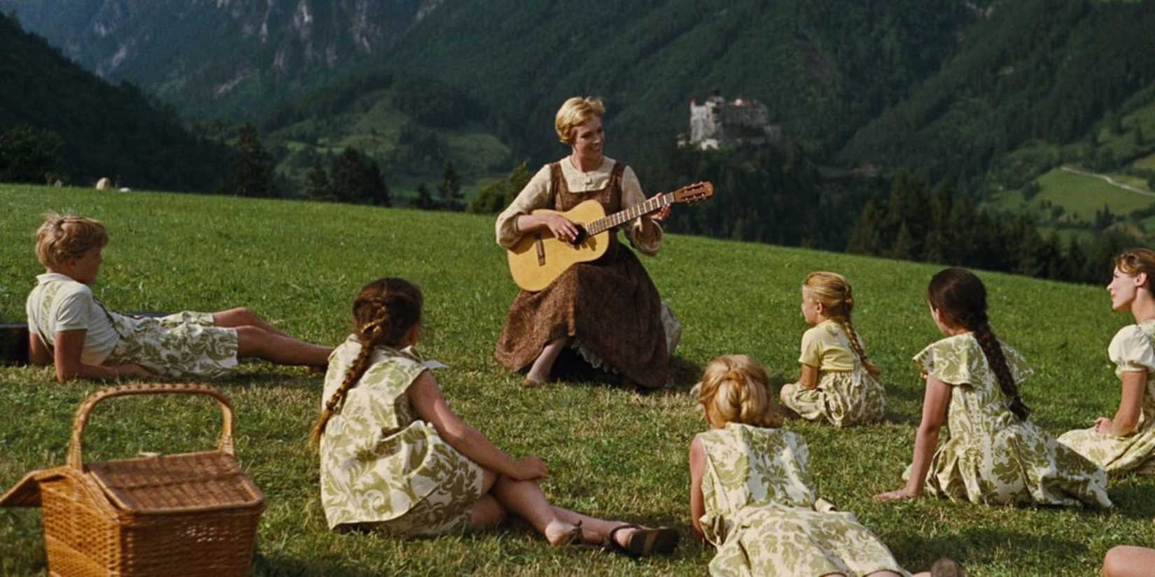 Julie Andrews as Maria plays a guitar as the children listen on a mountainside in The Sound of Music.