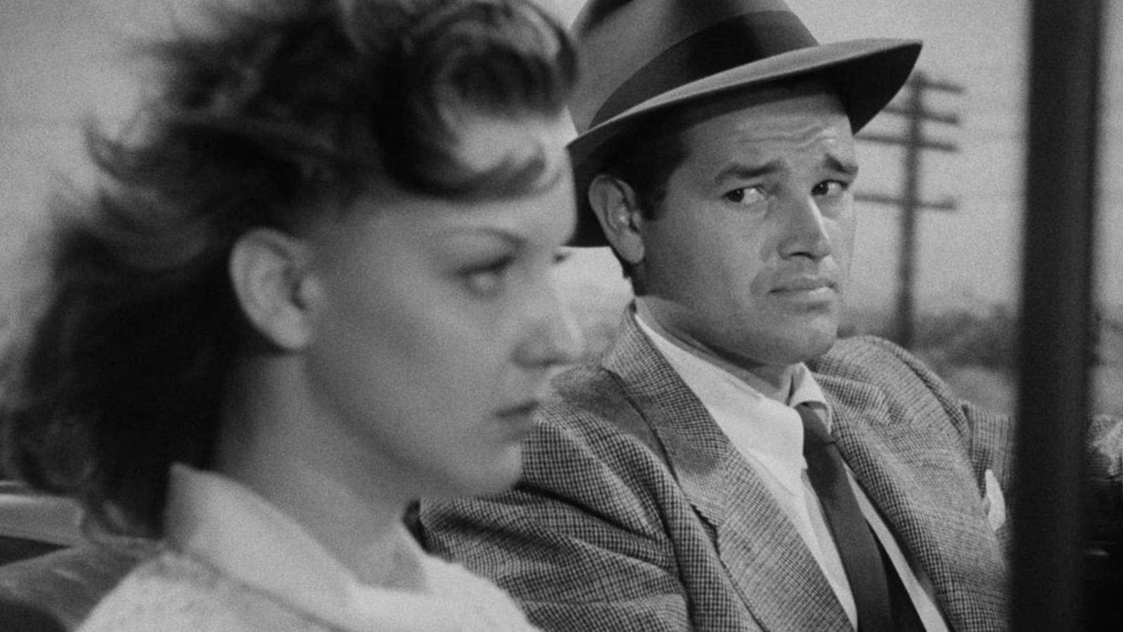 Tom Neal driving a car looking over at Ann Savage sitting in the passenger seat in Detour