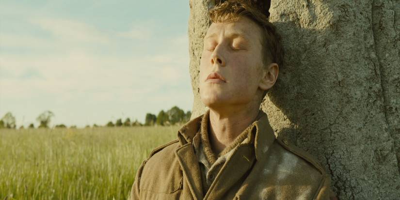 George Mackay as Will Schofield leans against a tree in an open field in 1917 (2019)