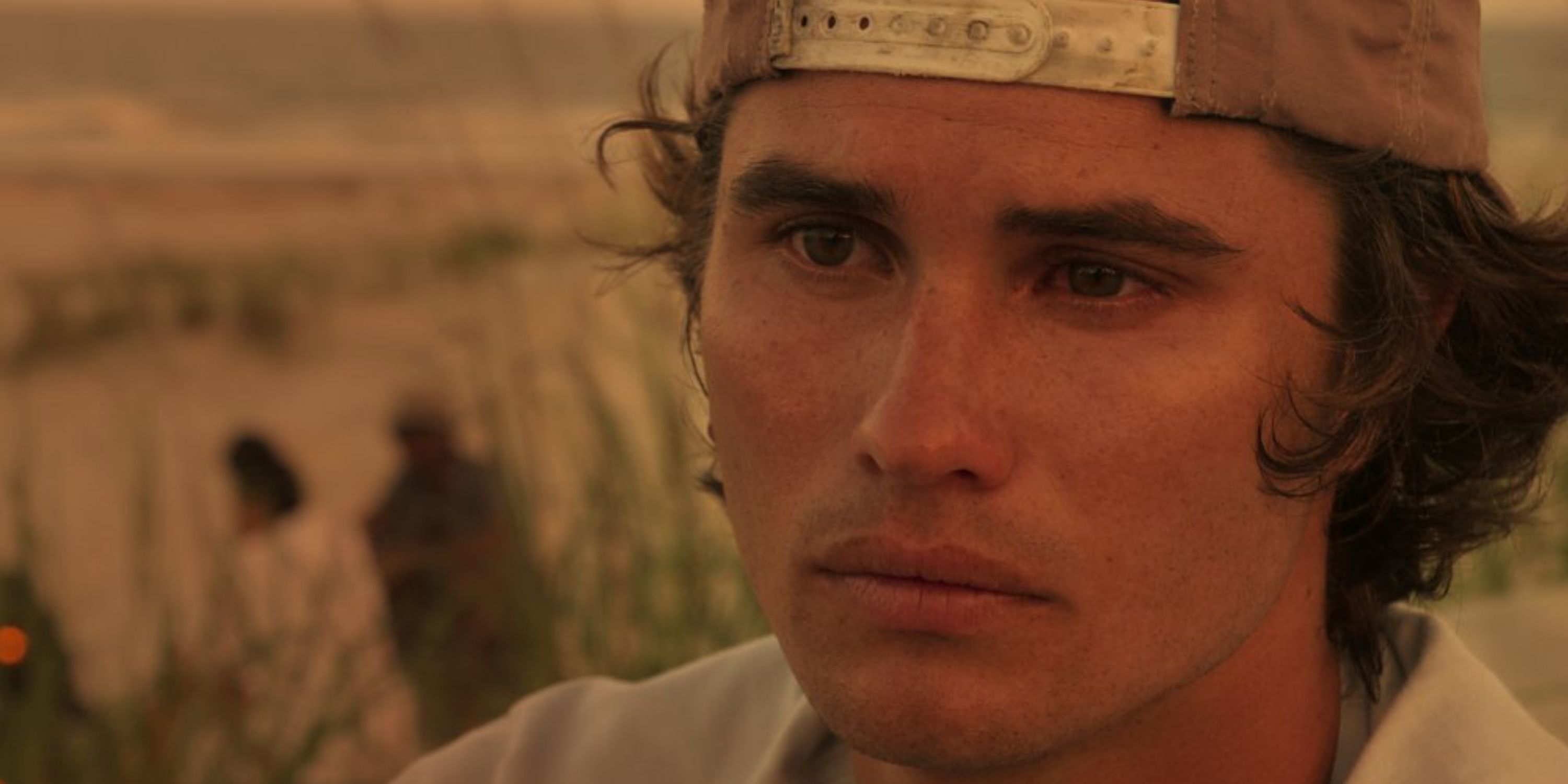 Chase Stokes as John B wearing a backward baseball cap and looking at a person offscreen solmenly in 'Outer Banks' Season 1