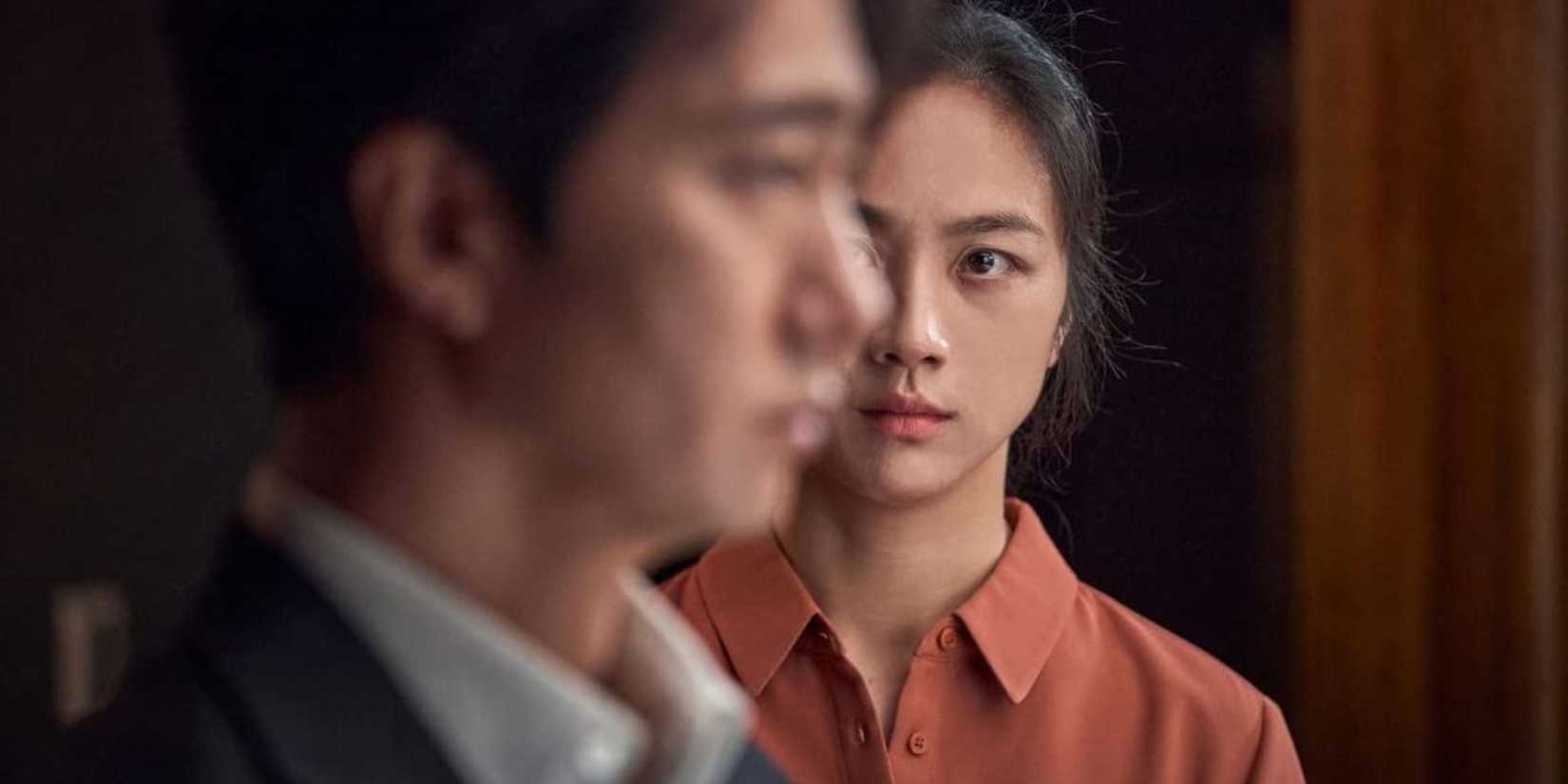 Tang Wei looking at Park Hae-il while he looks through a window in Decision to Leave.