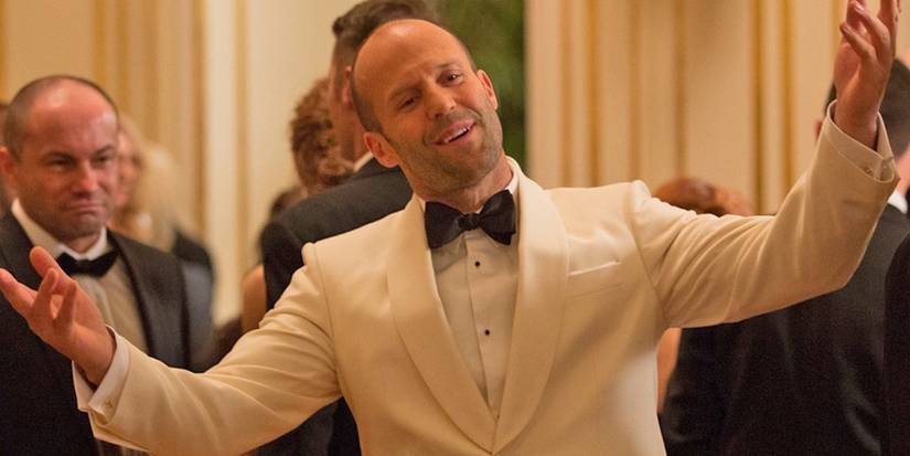 Jason Statham as Rick Ford smiling at a gala with his arms raised in Spy