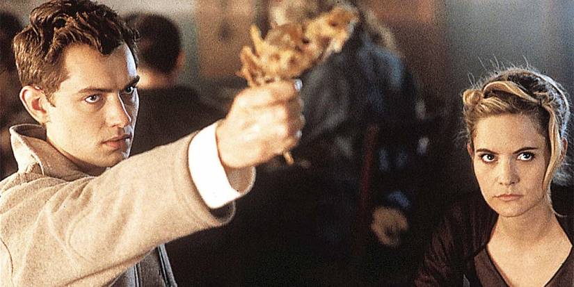 Jude Law as Ted aims his gun while Jennifer Jason Leigh as Allegra looks on in eXistenZ