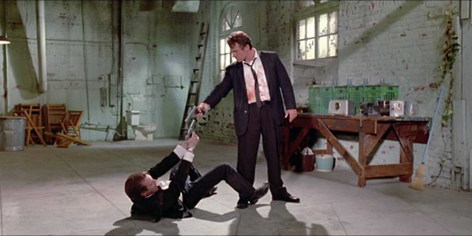 Mr. Orange wounded on the floor and Mr. White standing over him, both pointing guns at each other