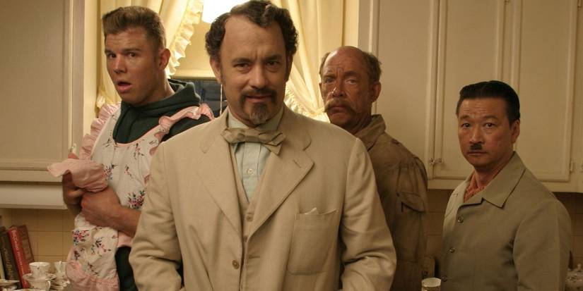Tom Hanks in a beige suit and bow tie looks ahead with three men behind him in The Ladykillers.