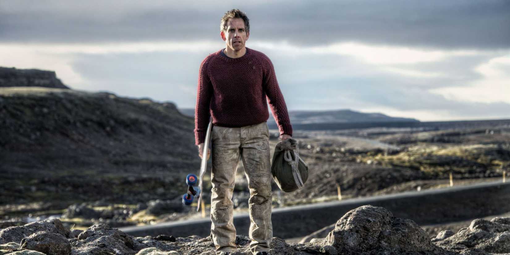Ben Stiller as Walter Mitty stands holding a skateboard and a travel bag in a remote landscape in The Secret Life of Walter Mitty.