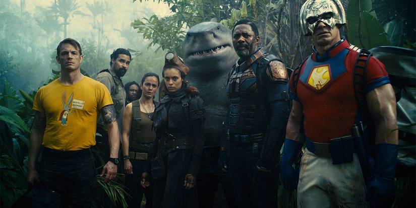 Ensemble cast of The Suicide Squad standing together in a forest