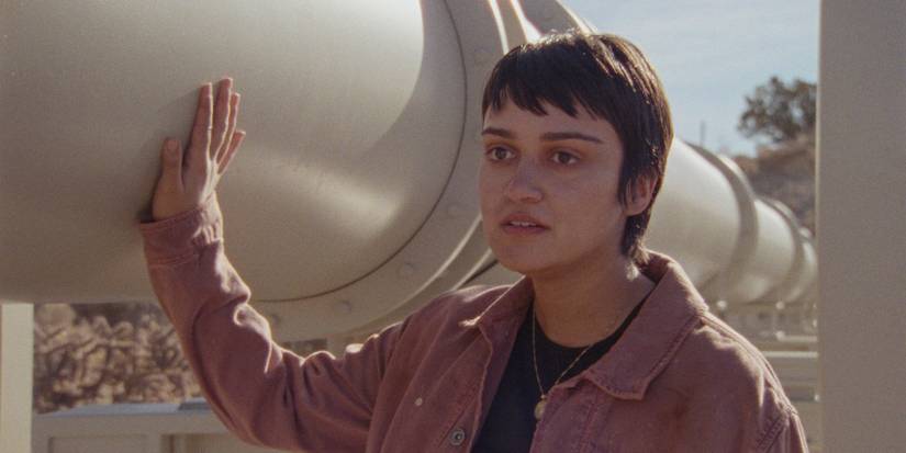 Ariela Barer as Xochitl standing next to a pipeline and looking ahead in How to Blow Up a Pipeline