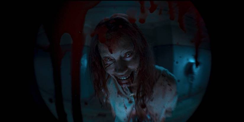 Alyssa Sutherland as deadite Ellie smiling creepily through the door peephole in Evil Dead Rise