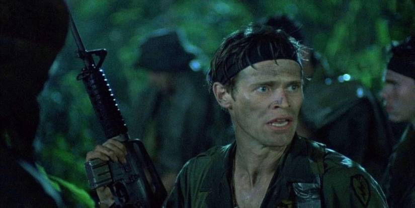 Sgt. Elias holding a gun and looking at the left in the jungle in Platoon (1986)