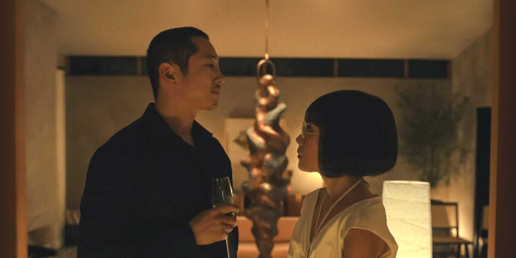 Steven Yeun and Ali Wong as Danny and Amy looking at each other, a fancy sculpture behind them, in Beef.