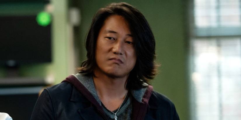 Close up of Sung Kang as Han looking to the left wearing a black leather jacket and hoodie in Fast X