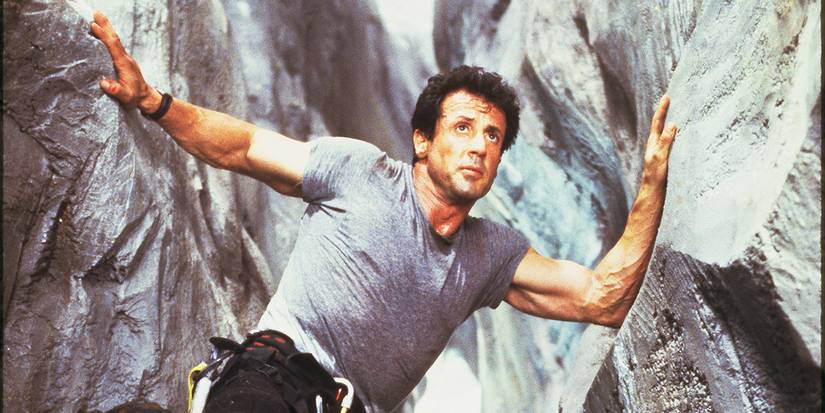 Sylvester Stallone hanging between two large rock walls in Cliffhanger