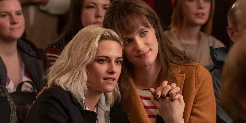 Kristen Stewart as Abby and Mackenzie Davis as Harper sit together in a scene from Happiest Season.