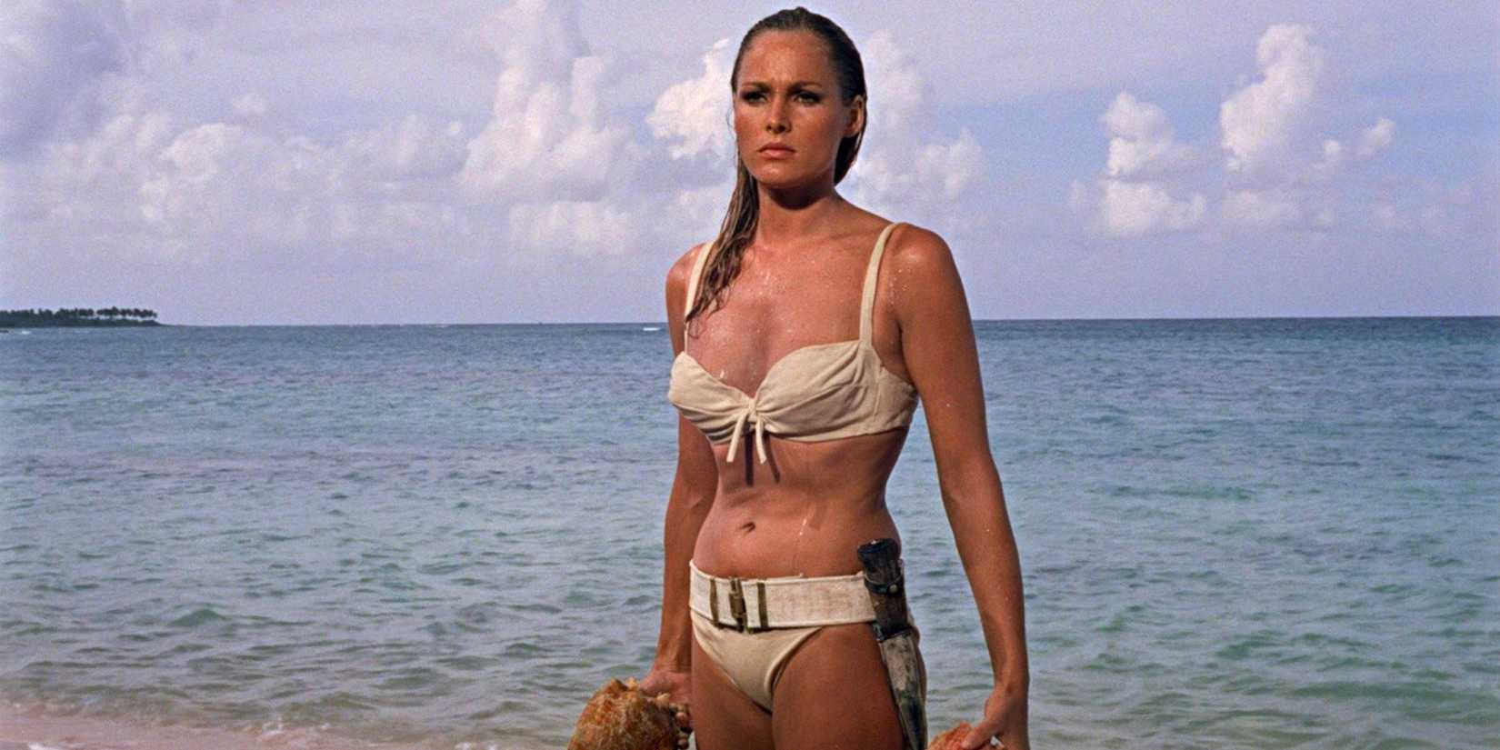 Shell diver Honey Ryder (Ursula Andress) stands on the beach in a bikini.