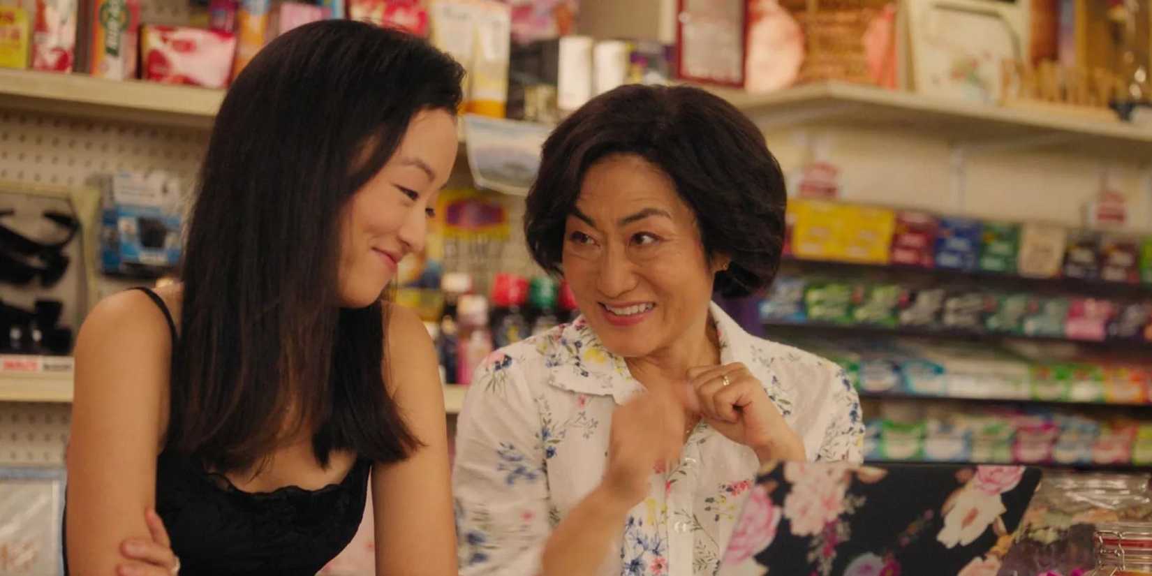 Andrea Bang as Janet smiles with Jean Yoon as Umma as they stand at the counter in Kim's Convenience.