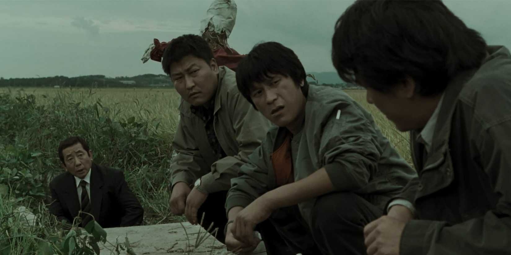 Three men crouching on an open field and exchanging glances in Memories of Murder