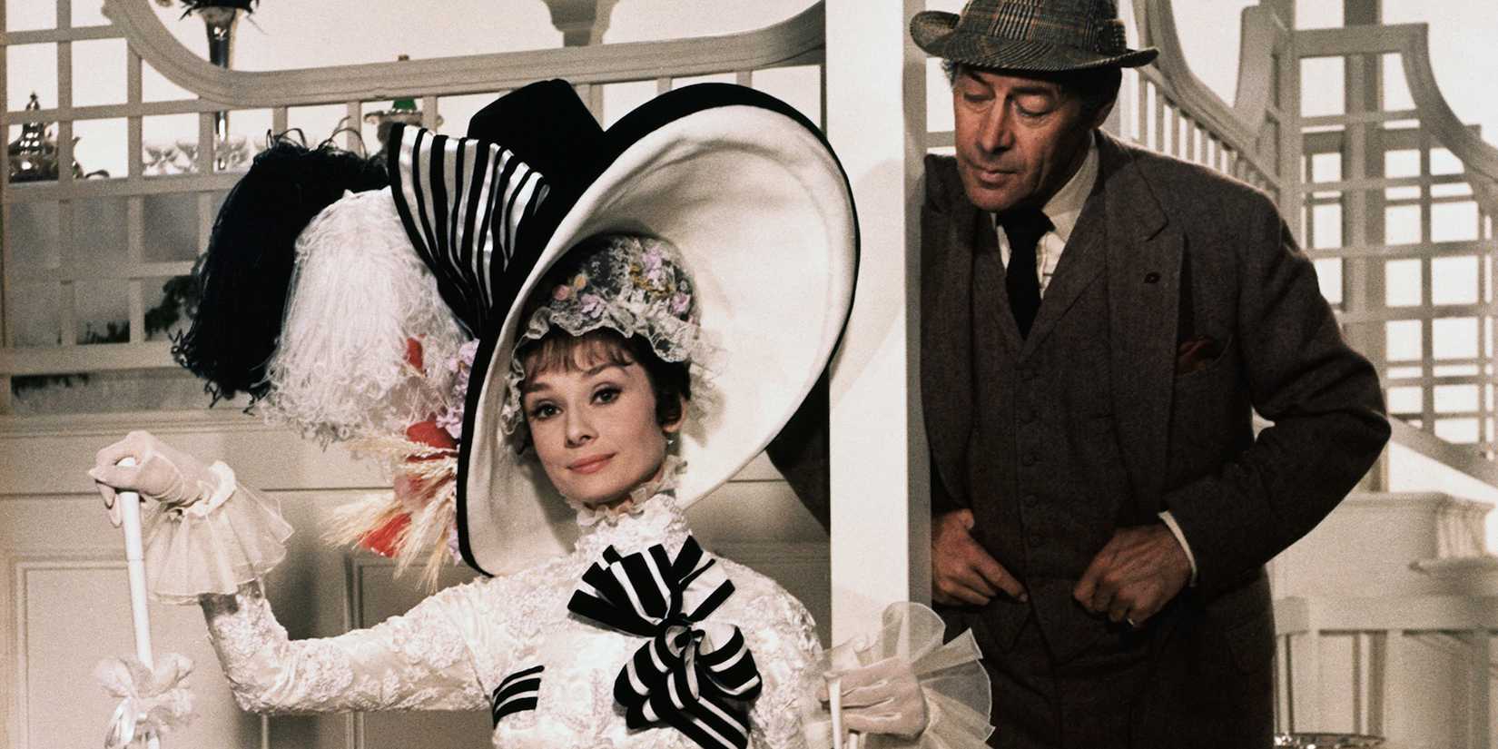 Professor Higgins standing behind Eliza, who's sitting on a chair, in My Fair Lady.