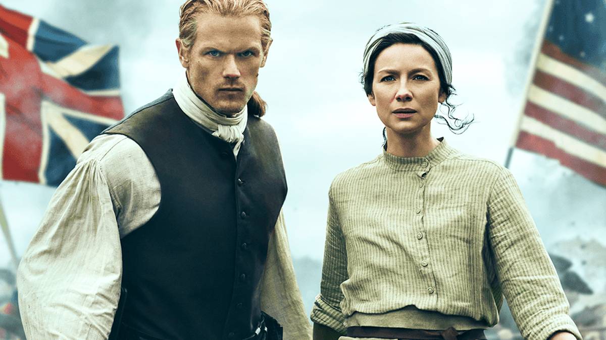 Sam Heughan and Caitriona Balfe on a battlefield in front of British and American flags in Outlander