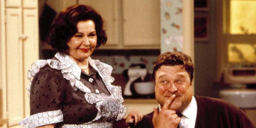 Roseanne Barr as Roseanne Conner and John Goodman as Dan Conner dressed up and smiling at the kitchen table in Roseanne Season 9