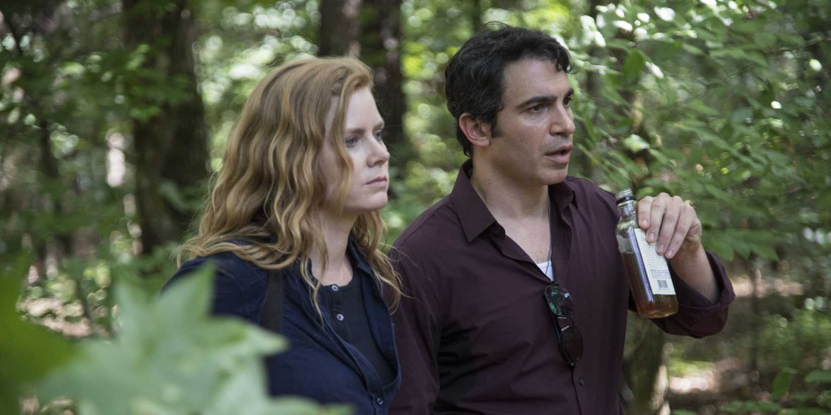 Camille (Amy Adams) and Richard (Chris Messina) in woods looking ahead and sharing a drink in Sharp Objects