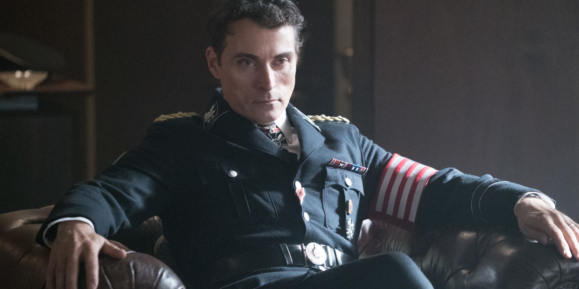 Rufus Sewell enquanto John Smith senta -se em uma cadeira em um uniforme militar no homem no castelo alto